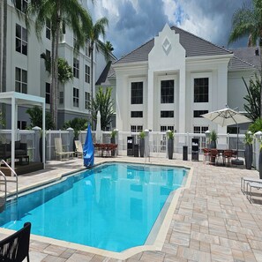 A swimming pool with a white fence, palm trees, and a building with large windows. - Revival Scottsdale Studios (Orlando)