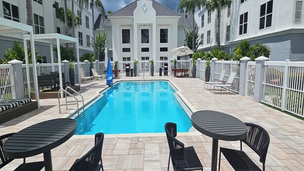 A swimming pool with lounge chairs and tables, surrounded by a white fence and palm trees. - Revival Scottsdale Studios (Orlando)
