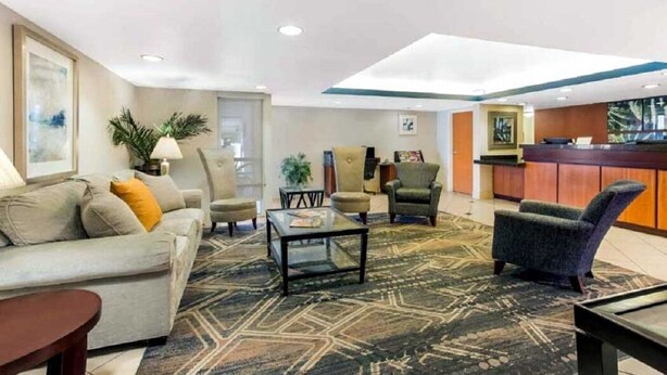 Eine Hotelhalle mit Empfangsschalter, einer Sitzecke mit Sofa und Sesseln sowie einem gemusterten Teppich.