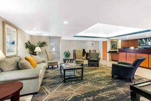 A hotel lobby with a reception desk, seating area with a sofa and chairs, and a patterned carpet. - Revival Scottsdale Studios (Orlando)