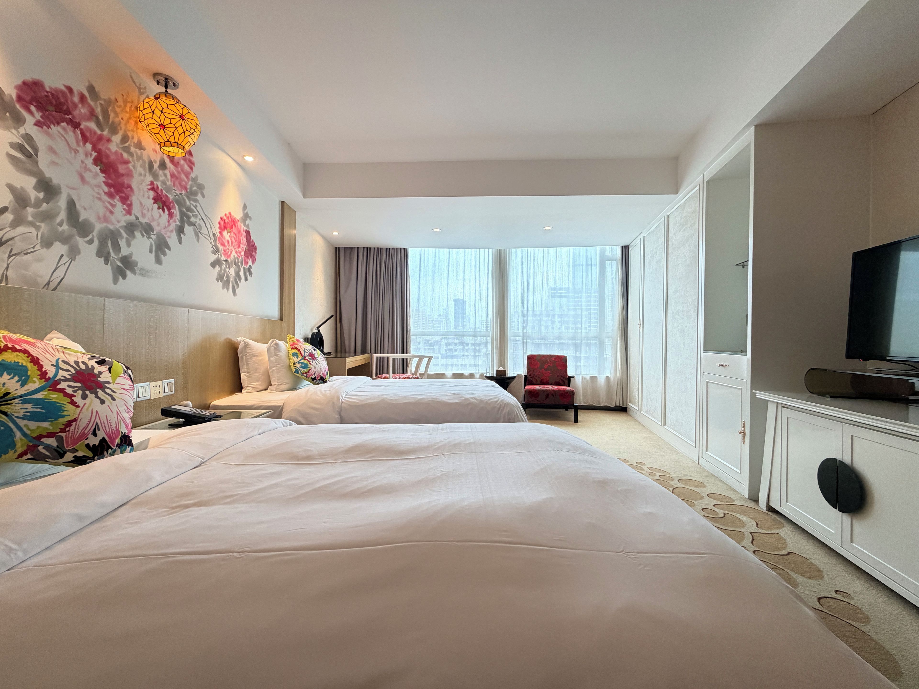 Ein Hotelzimmer mit zwei Betten, einem Fernseher, einem Sessel und Blick auf die Stadt.