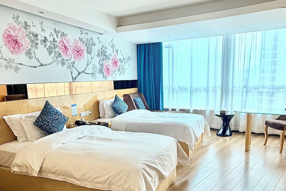 Ein Hotelzimmer mit zwei Betten, einem Schreibtisch, einem Stuhl und einem großen Fenster mit Vorhängen.