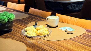Un comedor con mesas, sillas, una taza de café, un plato de cruasanes y una pequeña planta.