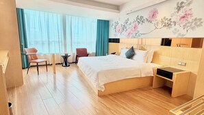 Habitación de hotel con cama, escritorio, silla, ventana con cortinas y decoración floral en la pared.