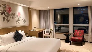 Habitación de hotel con una cama grande, un escritorio, una silla y vista a la ciudad de noche.