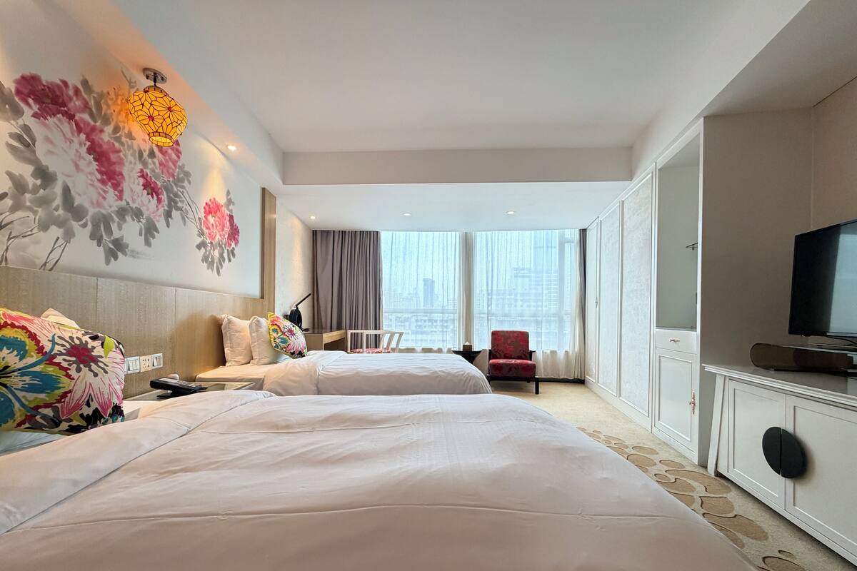 Ein Hotelzimmer mit zwei Betten, einem Fernseher, einem Sessel und Blick auf die Stadt.