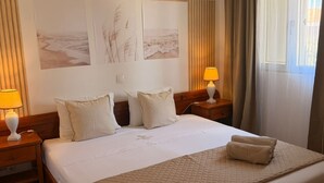 Une chambre d’hôtel avec un lit, deux tables de chevet avec des lampes, une couvre-lit matelassée et une vue sur la plage par la fenêtre.