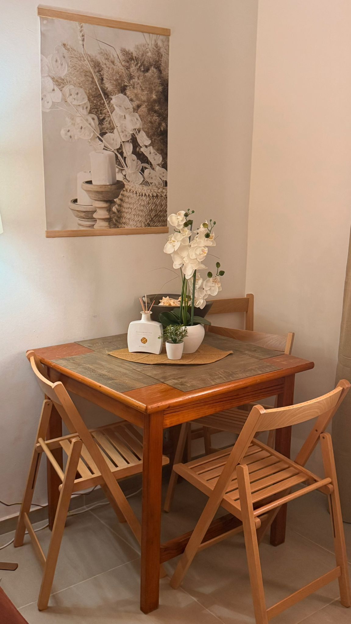 A dining table with chairs, a candle holder, a small potted plant, and a framed picture on the wall.