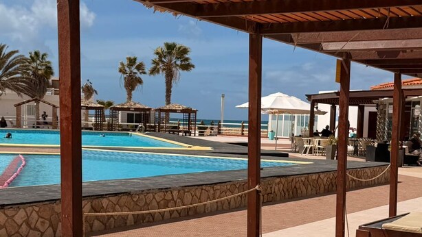 Un espace piscine doté de chaises longues, d’une pergola et offrant une vue sur l’océan.