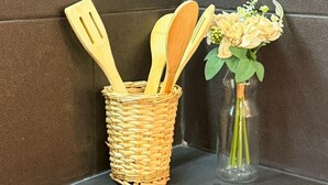 Un coin cuisine avec un panier en osier contenant des ustensiles en bois, un vase en verre avec des fleurs et une plaque de cuisson.
