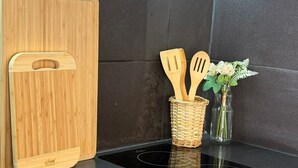 Une cuisine avec un plan de travail noir, une planche à découper en bois, un panier tressé contenant des ustensiles et un vase avec des fleurs.