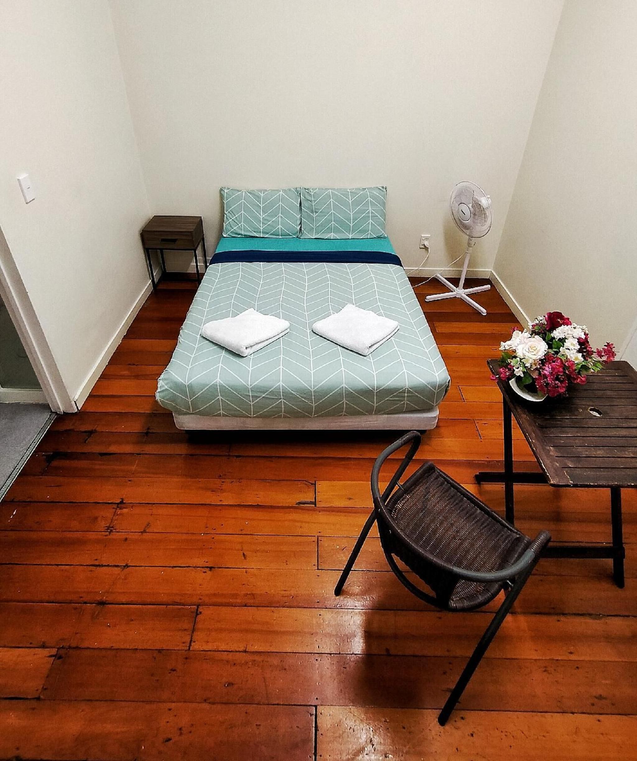 A small room with a bed, a chair, a small table, and a fan.