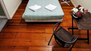 Ein kleines Zimmer mit einem Bett, einem Sessel, einem kleinen Tisch und einem Ventilator.