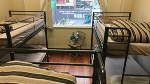 Ein Schlafsaalzimmer mit Etagenbetten, einem kleinen Tisch mit Stuhl und einem Fenster mit Blick auf Gebäude.