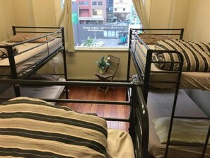 A dormitory room with bunk beds, a small table with a chair, and a window with a view of buildings. - Surf 'N' Snow Backpackers (Auckland)