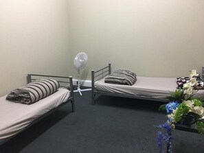 A small, single-room accommodation with two single beds, a standing fan, and a small table with a vase of flowers. - Surf 'N' Snow Backpackers (Auckland)