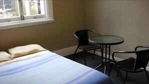 Ein Zimmer mit einem Bett, zwei Stühlen, einem kleinen runden Tisch und einem Fenster mit Blick auf Gebäude.