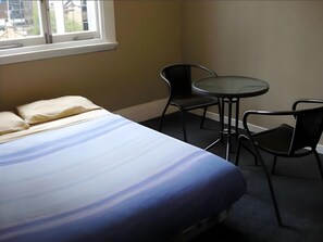 A room with a bed, two chairs, a small round table, and a window with a view of buildings. - Surf 'N' Snow Backpackers (Auckland)