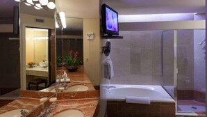 Un baño con dos lavabos, un espejo, un televisor, un ventilador y una zona de ducha.