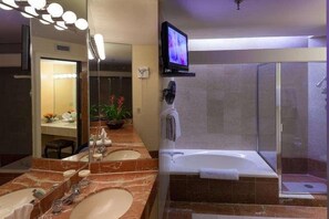 Ein Badezimmer mit zwei Waschbecken, einem Spiegel, einem Fernseher, einem Ventilator und einer Duschkabine.