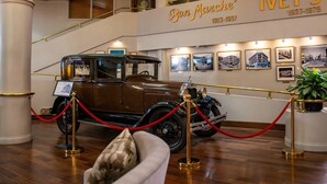 A vintage car on display, a staircase, and a wall with framed pictures and a sign reading 'Bon Marche' 1937-1975'.