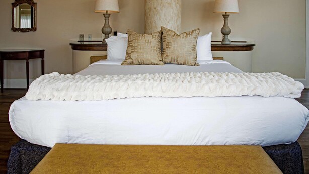 A large bed with white bedding, two bedside lamps, a mirror, and a wooden nightstand.