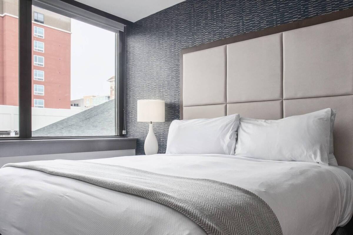 Ein Hotelzimmer mit einem großen Bett, einem Kopfteil, einem Fenster und einer Lampe.