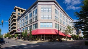 A multi-story hotel with a corner entrance, large windows, and a red awning.