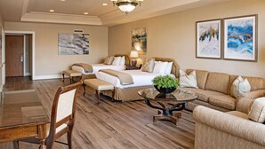A hotel room with a large bed, two bedside tables, a sofa, a dining table, and a small coffee table.