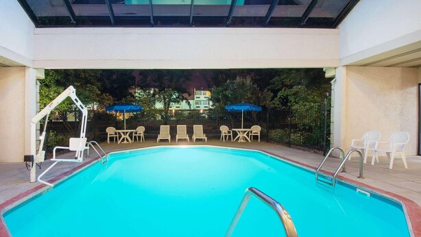 An indoor swimming pool with a clear view of the surrounding area, including a covered seating area with chairs and umbrellas.