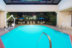 Una piscina interior con vistas despejadas del entorno, incluyendo una zona de estar cubierta con sillas y sombrillas.