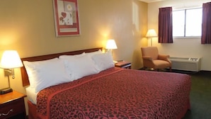 A hotel room with a bed, two bedside lamps, a chair, a window with curtains, and a wall-mounted picture.