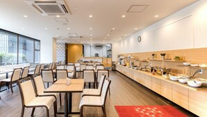 A modern dining area with tables and chairs, a kitchen in the background, and a red rug with Japanese characters. - APA Hotel Marugame-ekimae-odori (Marugame)