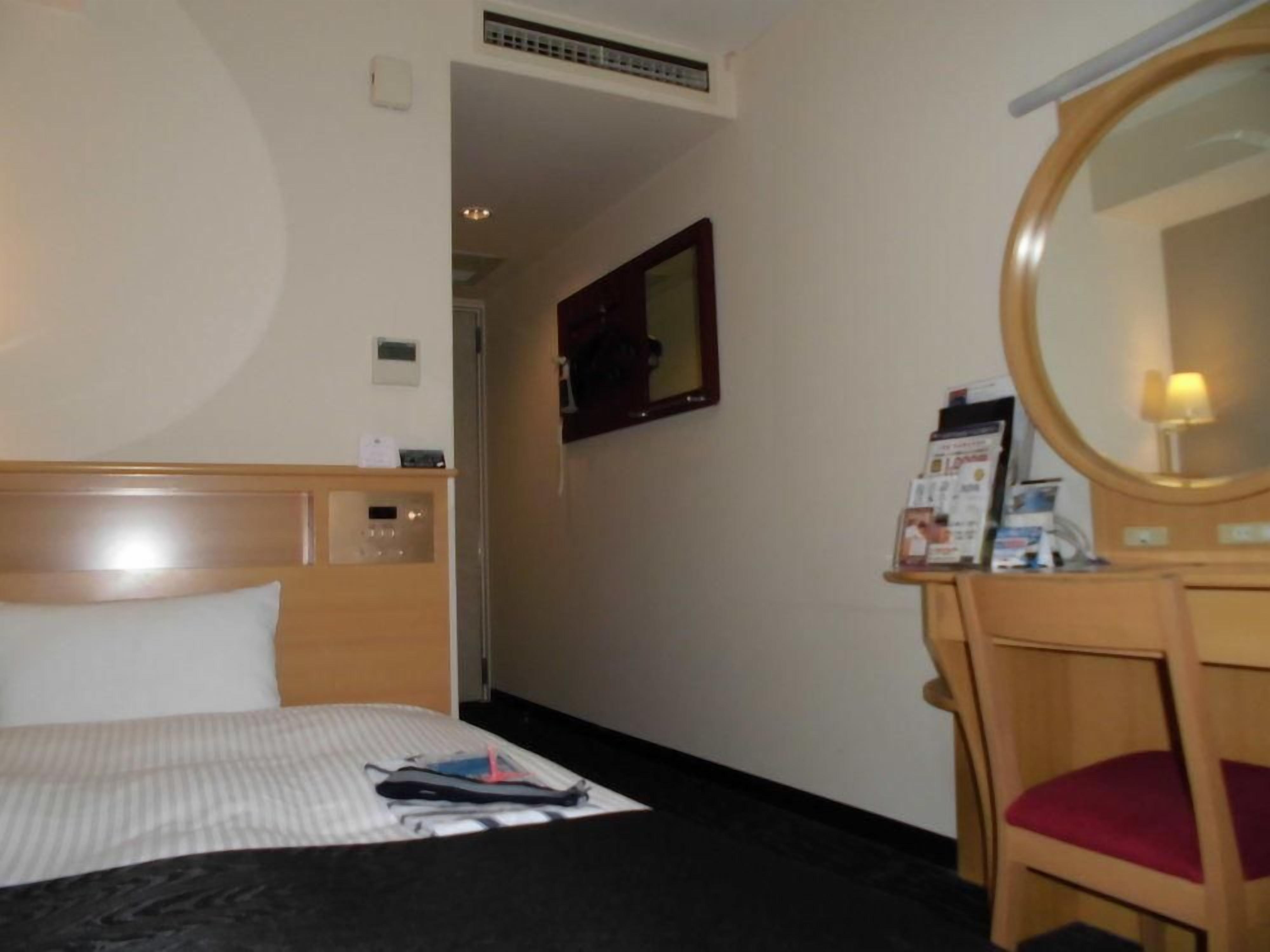 Una habitación de hotel con una cama, un escritorio de madera con un espejo y una mesita con un folleto.