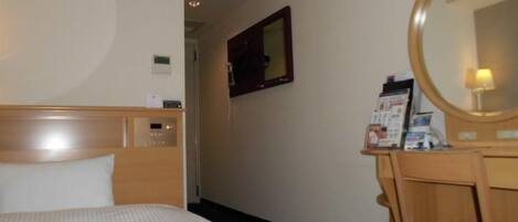 A hotel room with a bed, a wooden desk with a mirror, and a small table with a brochure.