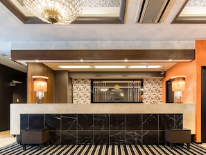 A hotel reception desk with a marble counter, two wall-mounted lamps, a chandelier, and a patterned wall. - APA Hotel Marugame-ekimae-odori (Marugame)
