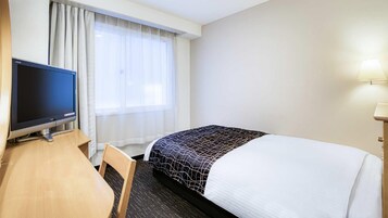 A hotel room with a bed, a desk with a television, a chair, and a window with curtains.
