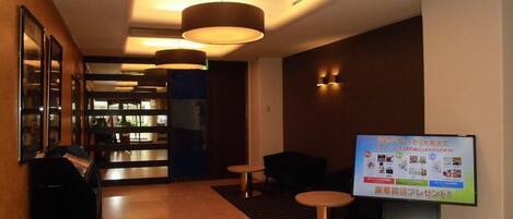 A hotel lobby with a reception desk, seating area, and a digital display board.