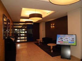 A hotel lobby with a reception desk, seating area, and a digital display board.