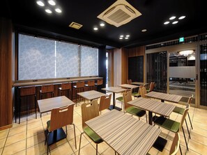 Un espace repas moderne avec des tables et des chaises en bois, une grande fenêtre ornée d’un motif de feuilles et un tableau noir accroché au mur.