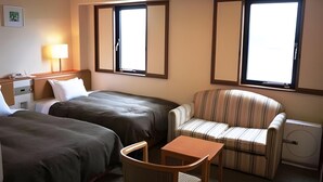 Een hotelkamer met twee bedden, een stoel, een klein tafeltje, een bureau met een lamp en twee ramen.