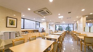 Un comedor con mesas y sillas, una zona de cocina y ventanas amplias.