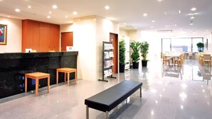 Zona de recepción con mostrador negro, taburetes de madera, un banco, plantas en macetas y una estantería.