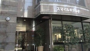 Entrada de hotel con fachada curva, un balcón con barandilla de metal y un cartel con caracteres japoneses.