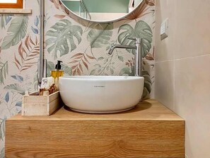 A bathroom with a white vessel sink, wooden countertop, and a mirror above it. - Hotel Donatella (Posada)