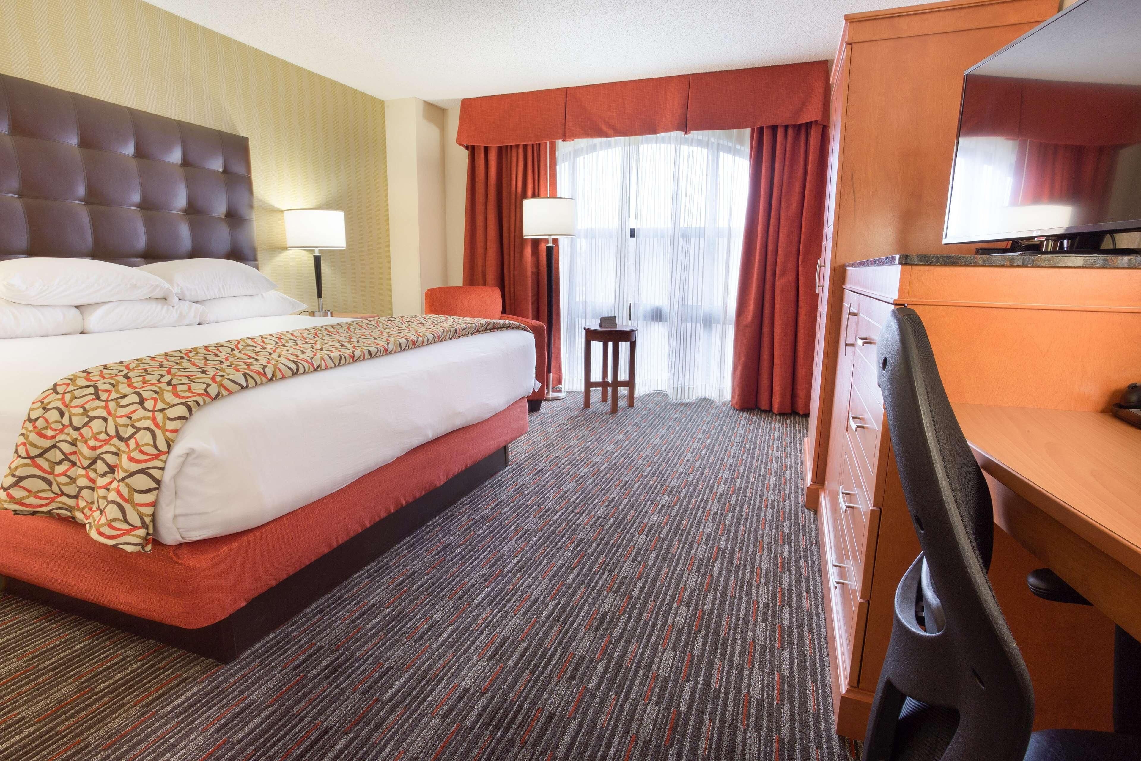 A hotel room with a large bed, a desk, a chair, a lamp, and a television.