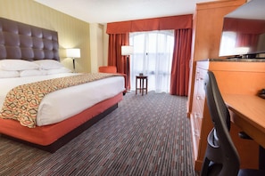 Ein Hotelzimmer mit einem großen Bett, einem Schreibtisch, einem Sessel, einer Lampe und einem Fernseher.