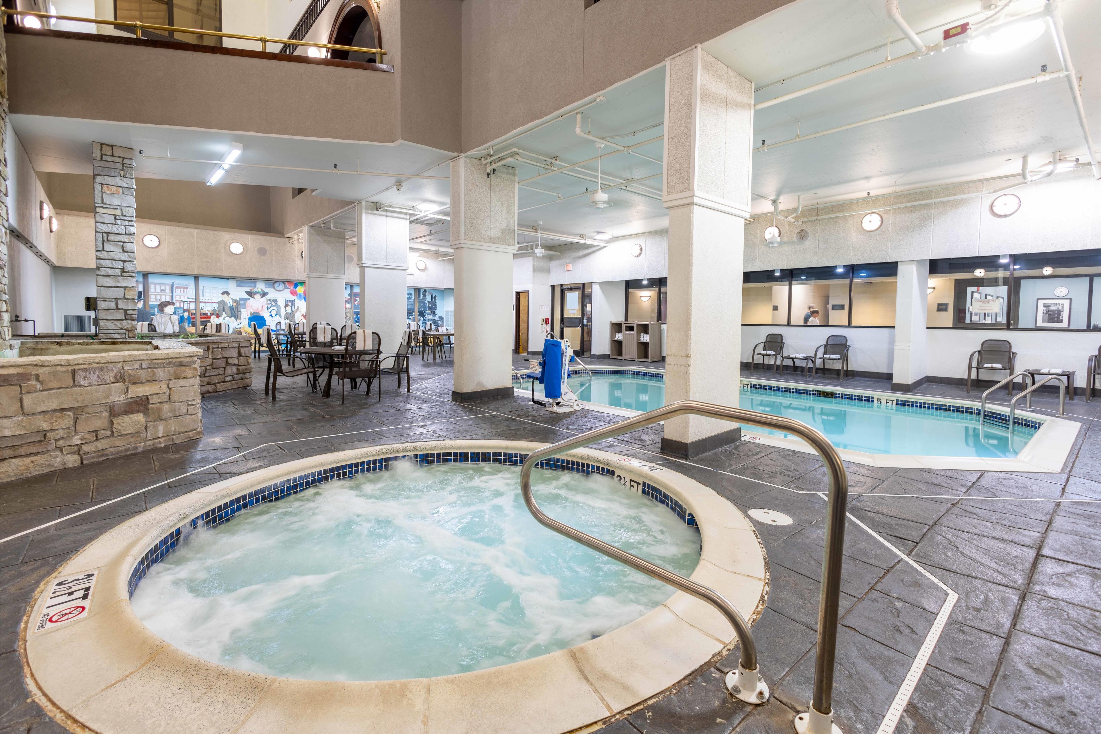 A hotel lobby with a hot tub, a pool, and a seating area with tables and chairs.