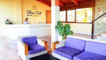 Zona de recepción con mostrador y una recepcionista, además de asientos morados.