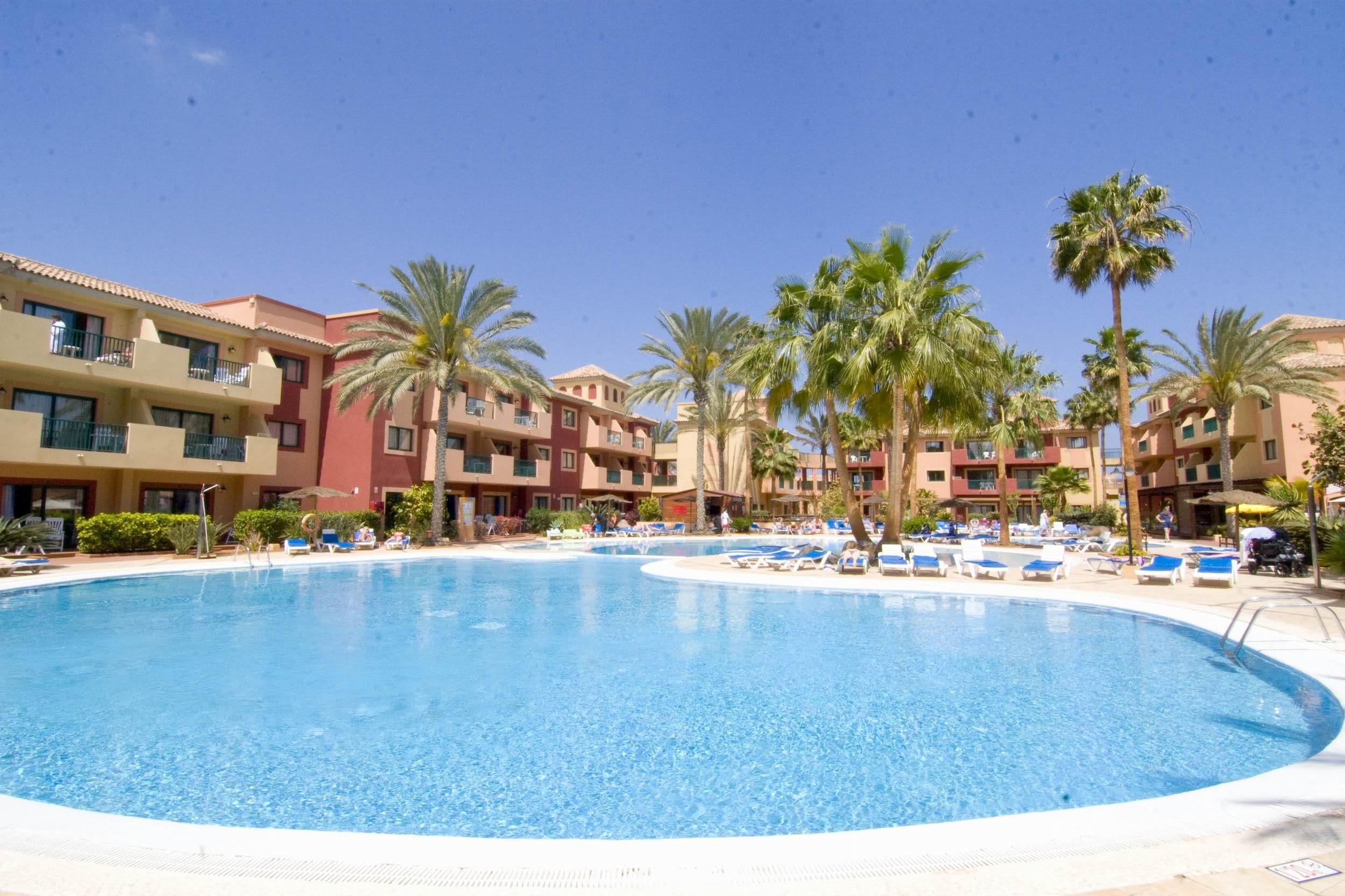 A swimming pool surrounded by palm trees and hotel buildings.
